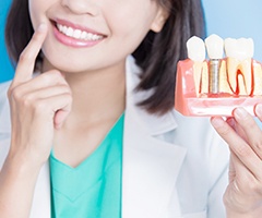 A woman holding a mold with a dental implant and pointing to her teeth