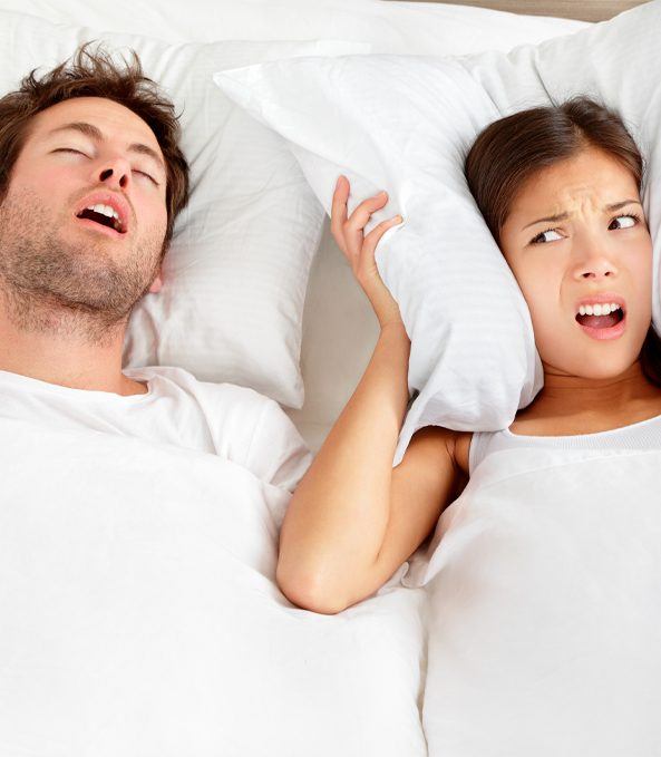 man snoring and woman holding pillow over her ears