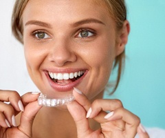 A woman smiling and holding a clear aligner.