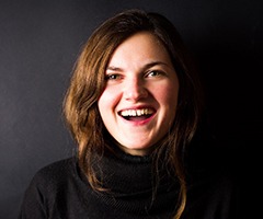 A young female with dark brown hair who is smiling with a gap between her two front teeth