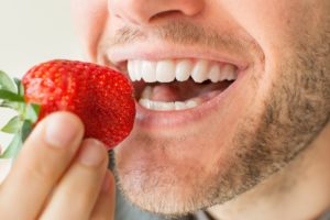 Closeup of man eating strawberry after teeth whitening in Charlottesville