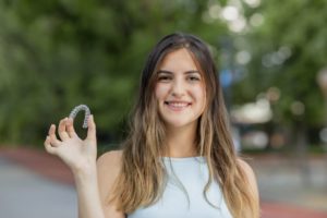 Smiling woman standing outside holding Invisalign in Charlottesville